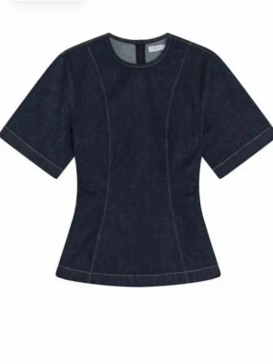 Mörkblå denim topp med kort ärm - Snygg mörkblå topp i denim med markerade sömmar och korta ärmar. Figurnära passform och rund halsringning. Nypris: 699kr