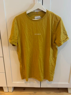 Gul t-shirt från Les Deux - Gul t-shirt från Les Deux med enkel design och vit text på bröstet. 