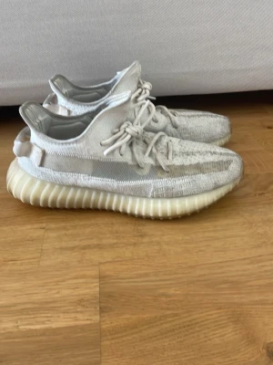 Yeezy Boost 350 V2 Cream White - Säljer ett par Adidas Yeezy Boost 350 V2 i färgen Cream White. Skorna har en stickad ovandel i vitt Primeknit, genomskinlig sidostrip och en tjock, ribbad sula i ljusbeige. Ikonisk siluett med snörning och låg profil. Perfekta för dig som gillar streetwear och hype sneakers.