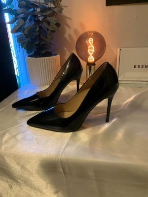 Svarta lackade stilettklackar - Säljer ett par svarta stilettklackar med spetsig tå och hög klack. Skorna är gjorda i glansigt lackmaterial och har en elegant, klassisk form som ger en riktigt snygg siluett.