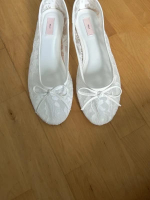 Vita spetsballerinaskor med rosett - Säljer ett par vita ballerinaskor från Nelly med romantisk spets och söt rosettdetalj framtill. Skorna har rundad tå och mjuk innersula för extra komfort. Perfekta för dig som gillar en feminin och stilren look. kom med pris förslag! 