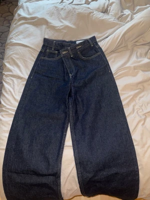 Mörkblå wide leg jeans från Gina Tricot - brand new with tags - Säljer ett par mörkblå jeans från Gina Tricot med riktigt breda ben och hög midja. Klassisk femficksmodell i kraftigt denimtyg med kontrastsömmar. Perfekta för dig som gillar en avslappnad och trendig look.