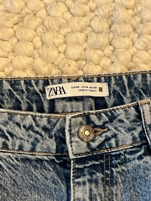 Blå  jeans från Zara - Säljer ett par blå jeans från Zara med hög midja och utsvängda ben. Jeansen har klassisk femficksdesign, knappgylf och är tillverkade i ett slitstarkt denimtyg. Perfekta för en avslappnad och trendig look.
