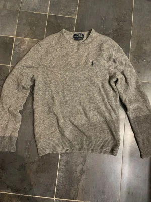 Stickad Ralph Lauren tröja - Stickad tröja från märket Ralph Lauren. Den är i relativt bra skick förutom ett hål jag hittat, som man ser på bilden. Annars är den i bra skick.
