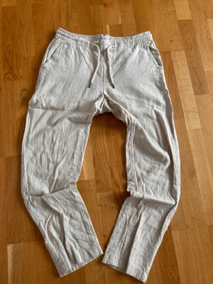 Beiga linnebyxor - Snygga beiga linnebyxor med avslappnad passform och elastisk midja med dragsko. Byxorna har sidfickor fram och två bakfickor med knapp. Perfekta för en chill och stilren look. 
