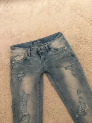 Ljusblå Lågmidjade Jeans med Slitningar & Hål - Hej! Säljer dessa superfina lågmidjade ljusblå jeansen med hål & slitningar då dom tyvärr inte kommer till någon användning av mig. Jeansen har blivit sparsamt använda, därav inga defekter & är i ett otroligt bra skick.  Verkligen helt perfekta jeans nu till sommaren om man vill ha ett par mer unika jeans med en fin färg. 🌞  Midjemåttet rakt över: 37-38cm  Innerbenslängden: 80cm Grenhöjden: 17cm  Om du skulle fundera över något så är det bara att höra av dig!