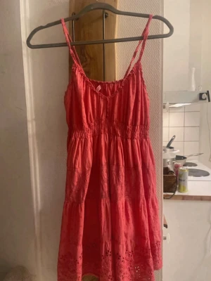 Rosa sommarklänning med broderi - Söt rosa kortklänning med smala axelband och v-ringad hals. Klänningen har fina broderade detaljer och hålmönster längst ner samt resår i midjan för en bekväm passform. Perfekt för varma dagar och ger en fräsch sommarkänsla.
