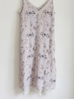 Floral pastel slip dress with lace trim - ISay  - Lovely and delicate vintage-style slip dress, perfect for spring and summer!  -Design & Pattern: Features a beautiful, subtle floral print with small blue, purple, and neutral flowers and delicate branches scattered across the fabric.  - Color: A soft, muted pastel lavender/lilac or light greyish-pink background tone that gives it a romantic, whimsical feel.