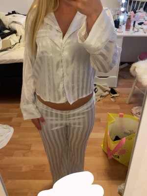 Vit satinpyjamas med ränder - Snygg tvådelad pyjamas i glansigt vitt satintyg med diskreta vertikala ränder. Pyjamas sett från Gina Tricot. dem säljs tillsammans men går även och köpa styckvis. Det finns separata annonser på min profil om man är intresserad av bara ett plagg. Settet är köpt för 300 kr , jag skulle ändå säga att den är använd fåtal gånger därav sätter jag priset på 200 kr. Båda delarna är från Gina Tricot i storlek 146/152.
