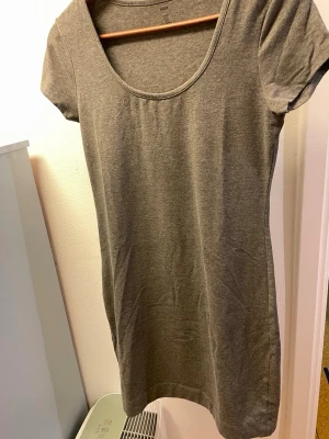 Grå kortärmad bomullsklänning - En enkel och stilren grå klänning i mjuk bomull med rund halsringning och korta ärmar. Perfekt för en avslappnad look och lätt att matcha med olika accessoarer.