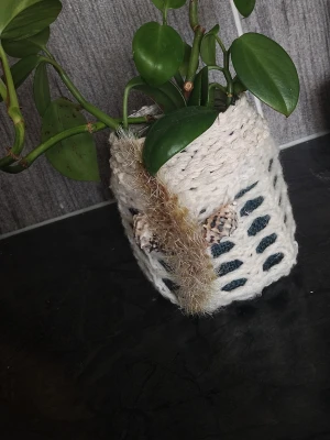 Handgjord virkad kruka med dekoration - Unik handgjord kruka med virkat vitt överdrag och dekorativa detaljer som fjädrar och garn. Perfekt för att ge en personlig touch till ditt rum. Passar mindre växter och har ett boho-inspirerat utseende.
