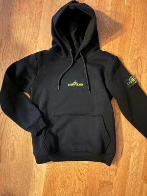 Svart hoodie från Stone Island - Tja! Säljer en Snygg svart hoodie från Stone Island med gul logga på bröstet och stort tryck på ryggen i vitt, gult och grått, eftersom den var för liten för mig, därmed är den inte använd! 