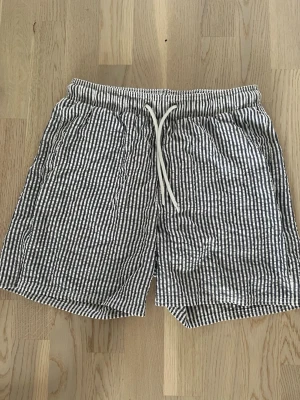 Snygga badshorts  - Passar mig jag är 177 Säljer ett par randiga shorts i svart och vitt med bekväm snörning i midjan. Shortsen har avslappnad passform och är tillverkade i ett lätt bomullstyg, perfekta för varma dagar. Två sidofickor och elastisk midja för extra komfort.