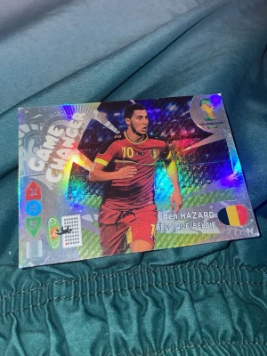 Game Changer fotbollskort Eden Hazard - Säljer ett glittrigt samlarkort med Eden Hazard från Belgien, märkt 'Game Changer'. Kortet har holografisk yta, färgglada detaljer och visar Hazard i röd matchtröja med nummer 10. Perfekt för dig som samlar på fotbollskort eller gillar fotboll.