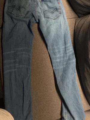 Ljusblå raka jeans med slitningar - Säljer ett par ljusblå jeans med raka ben och diskreta slitningar över låren. Jeansen har klassiska bakfickor med dekorativa sömmar och normal midja. Perfekta för en avslappnad och trendig stil.