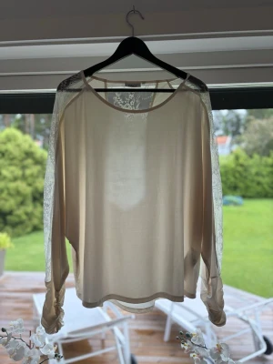 Vit blus med spetsdetaljer - Säljer en beige blus med transparenta spetsärmar och spetsinfällning upptill. Blusen har rund halsringning och ett lätt, flödande tyg som ger en luftig känsla. Perfekt för dig som gillar romantiska detaljer och en feminin stil.