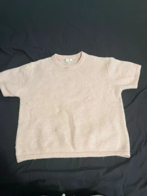 Ljusrosa stickad t-shirt - Säljer en ljusrosa stickad t-shirt med korta ärmar och rund halsringning. Tröjan har en enkel och avslappnad passform, perfekt för lager på lager. Materialet känns mjukt och bekvämt mot huden.