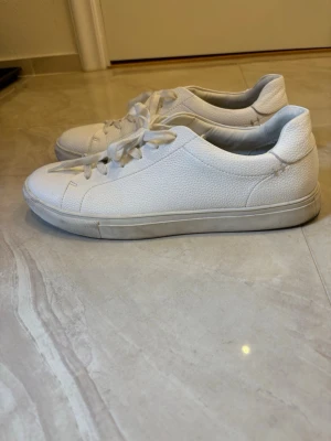 Vita sneakers - Stilrena vita sneakers med lågt skaft och snörning. Tillverkade i strukturerat skinnmaterial med vit sula och minimalistisk design. Perfekta för dig som gillar en clean och enkel look.