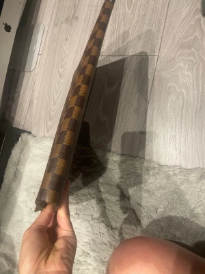 Brun dataväska i rutigt mönster - Snygg kuvertväska i brunt och beige rutigt mönster med dragkedja upptill. Väskan är tunn och rektangulär, perfekt för att bära det viktigaste. Tillverkad i ett tåligt material med klassisk look.