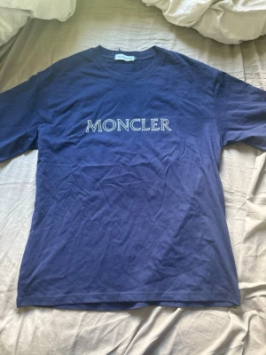 Blå Moncler t-shirt med logga - Snygg blå t-shirt från Moncler med klassisk logotyp tryckt på bröstet. T-shirten har rund halsringning och korta ärmar. Perfekt för dig som gillar stilrena och exklusiva plagg.