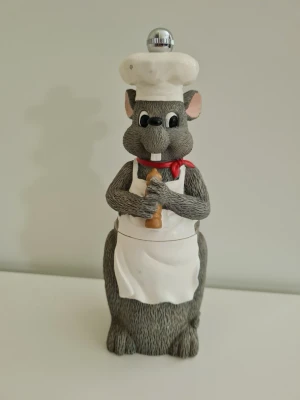 Vintage Pepparkvarn i form av en kockråtta - Pepparkvarn i form av en grå råtta klädd som en kock med vit kockmössa och vitt förkläde. Råttan håller i en liten kavel. Pepparkvarnen är manuell och fylls på underifrån. Höjd 17cm