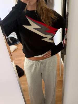 Svart tröja med blixtmönster från Zadig - Cool svart tröja från Zadig med ett stort blixtmönster i vitt, grått och rött över bröstet och ena ärmen. Tröjan har rund halsringning och långa ärmar. 