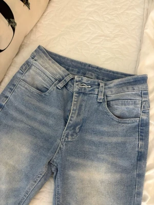Ljusblå bootcut jeans - Säljer ett par ljusblå bootcut jeans med slitna detaljer och klassisk femficksmodell. Jeansen har hög midja och är tillverkade i mjukt denimtyg med stretch. Perfekta för en avslappnad och trendig look.