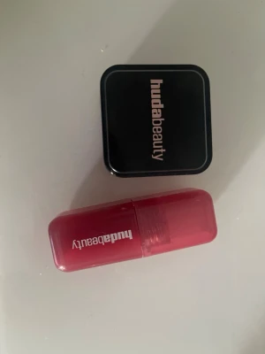 Huda Beauty Cherry Blossom Cake Rouge - Rouge från Huda Beauty i färgen Cherry Blossom Cake. Kommer i en kompakt fyrkantig dosa med svart lock och vit logga. Färgen är en intensiv rosa nyans som ger kinderna ett fräscht och livfullt glow. Perfekt för dig som vill ha en poppig och modern look.Jag har bara provat dem en enda gång. Jag säljer båda f 550kr 