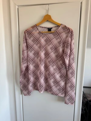 Rutig långärmad topp från Lindex - Säljer en rutig långärmad topp från Lindex i ljusa rosa och beige toner. Toppen har en rund halsringning och ett mjukt, stretchigt material som känns skönt mot huden. Perfekt för dig som gillar en avslappnad men ändå trendig stil.