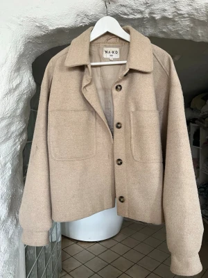 Beige oversized kappa från NA-KD - Stilren beige overshirt från NA-KD med stora framfickor och klassisk krage. Jackan har knappar framtill och är gjord i ett mjukt ull-liknande material. Perfekt för lager på lager och enkel att matcha med olika outfits. Lite knopprig o missfärgning som knappt syns vid ärmen