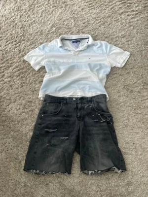 Svarta slitna jeansshorts - Svarta jeansshorts med slitna detaljer och råa kanter. Klassisk femficksmodell med knapp och dragkedja framtill. Perfekta för en avslappnad och cool stil.