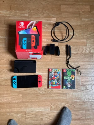 Nintendo Switch OLED + 2 Spel (Mario Odyssey & Luigi's Mansion 3 - Säljer ett komplett Nintendo Switch OLED-paket i absolut nyskick! Detta är den nyare modellen med den mycket bättre och större skärmen. Allt fungerar helt felfritt och är sparsamt använt.Det som ingår i paketet:Nintendo Switch OLED-konsolOriginalkartongTV-docka, strömkabel och HDMI-kabelJoy-Con Grip (handkontroll) och handledsremmarFysiskt spel: Super Mario Odyssey (med fodral)Fysiskt spel: Luigi's Mansion 3 (med fodral)Kan skickas säkert och spårbart direkt med Vinteds frakt! Price is firm.