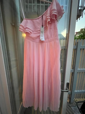 Ljusrosa oneshoulder klänning Gynning - Säljer en ljusrosa oneshoulder klänning från Carolina Gynning för Bubbleroom. Klänningen har volang upptill och plisserad kjol, vilket ger en romantisk och luftig känsla. Perfekt för sommarens alla tillfällen!