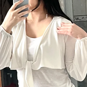 Vit Bolero Jacka - Vit bolerotopp i croppad modell med långa ärmar och knyt framtill. Från Boohoo och aldrig använd!