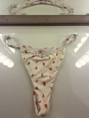 Ny bikiniunderdel med blommigt mönster i strl M - Supersöt bikiniunderdel i vit ( off-white)ribbad stretch med små rosa blommor och gröna blad. Spetskant upptill och smala sidor ger en romantisk och feminin känsla. Perfekt för stranddagar och sommarhäng. Bikiniunderdelen är helt oanvänd, men saknar prislapp!