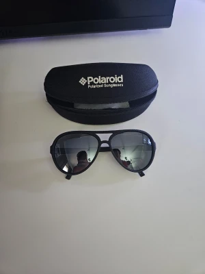 Svarta Polaroid pilot-solglasögon - Snygga svarta pilot-solglasögon från Polaroid med polariserade linser. Klassisk aviator-modell med spegelglas och svart båge. Kommer med originalfodral som skyddar glasögonen när du inte använder dem. Priset kan diskuteras