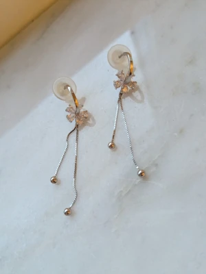 Silvriga örhängen med blommor och kedjor - Säljer ett par eleganta silvriga örhängen med gnistrande blomdetaljer upptill och två tunna kedjor som avslutas med små kulor. Örhängena har en modern och stilren design som ger en lyxig känsla. Perfekta för dig som gillar unika accessoarer.