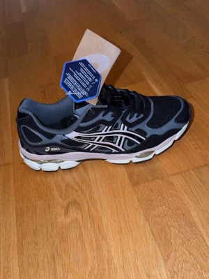 Svarta ASICS sneakers med meshdetaljer - Snygga svarta sneakers från ASICS med vita och grå detaljer. Skorna har en sportig design med meshpaneler för bra ventilation och en rejäl, stötdämpande sula. Perfekta för dig som gillar streetwear och vill ha bekväma skor till vardags. Klassisk ASICS-logga på sidan.