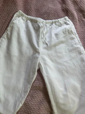 linnebyxor - Säljer ett par vita linnebyxor från Kappahl med resår  i midjan. Byxorna har raka ben och sidofickor, perfekta för en avslappnad och stilren look. Materialet är svalt och luftigt linne som passar bra till sommaren.