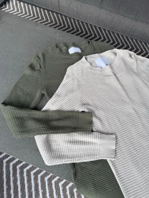 Två stickade tröjor i grönt och beige - Säljer två stickade tröjor i en snygg, grovstickad struktur. En är olivgrön och den andra är ljusbeige. Båda har rund halsringning, långa ärmar och ribbade muddar. Perfekta för lager på lager och chill stil.