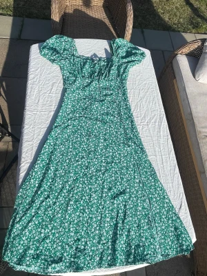 Grön långklänning med slits nertill - Säljer en fin långklänning med slits nertill på vänster sida i storlek M. Den har knytning i bysten och har puffiga armar. Knappt använd🤩☺️
