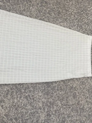 Vit långkjol med rutigt mönster - Säljer en vit långkjol med diskret rutigt mönster. Kjolen har en rak passform och är gjord i ett mjukt, lätt material som känns skönt mot huden. Perfekt för dig som gillar stilrena och enkla plagg med en twist.