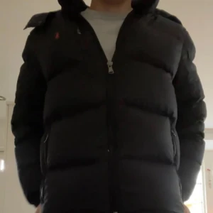 Ralph Lauren vinterjacka - Säljer en stilren svart dunjacka från Ralph Lauren. Perfekt för kyligare dagar med sin pufferdesign som håller värmen. En klassisk och tidlös modell för garderoben.