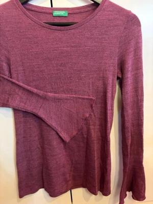 Vinröd/lila tröja med utsvängda ärmar - Säljer en vinröd/lila tröja från United Colors of Benetton med snygga utsvända ärmar. Tröjan är stickad i ett mjukt, tunt material och har en enkel, figursydd passform. 