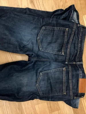 Mörkblå Acne Studios jeans - Mörkblå jeans från Acne Studios med klassisk femficksdesign och raka ben. Jeansen har kontrastsömmar och en snygg läderpatch med Acne-logga bak i midjan. Tillverkade i slitstark denim för en tidlös look.