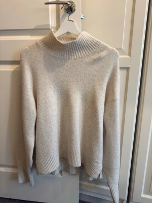 Beige stickad tröja från Uniqlo - Mysig beige stickad tröja från Uniqlo med hög ribbad polokrage och breda ribbade muddar vid ärmslut och nederkant. 