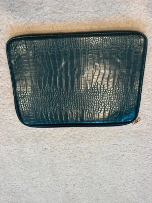 Mörkgrön laptopfodral med krokoprägling - Stilrent laptopfodral i mörkgrönt konstläder med krokodilpräglad yta och dragkedja. Perfekt för att skydda din dator med en trendig look. Passar de flesta laptops och ger en lyxig känsla till din vardag.