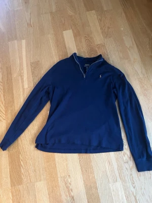 Marinblå tröja från Polo Ralph Lauren - Snygg marinblå långärmad tröja från Polo Ralph Lauren med halv dragkedja och liten broderad logga på bröstet. Klassisk och stilren design, perfekt till jeans eller chinos. Tillverkad i mjukt bomullsmaterial för skön känsla. Storlek 170,Använd max 5 gånger.
