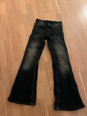 Mörkblå bootcut jeans Cheap Monday - Säljer ett par mörkblå bootcut jeans från Cheap Monday med slitningar och snygg tvätt. Jeansen har klassisk femficksmodell, låg midja och ett stort vitt märke med döskalle på bakfickan. Perfekta för dig som gillar retrostil och breda ben.