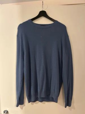 Blå stickad tröja från Oscar Jacobson - Snygg blå stickad tröja från Oscar Jacobson med rund halsringning och ribbade muddar vid ärmslut och nederkant. Tillverkad i Italien och har en klassisk, avslappnad passform som funkar till många olika stilar.